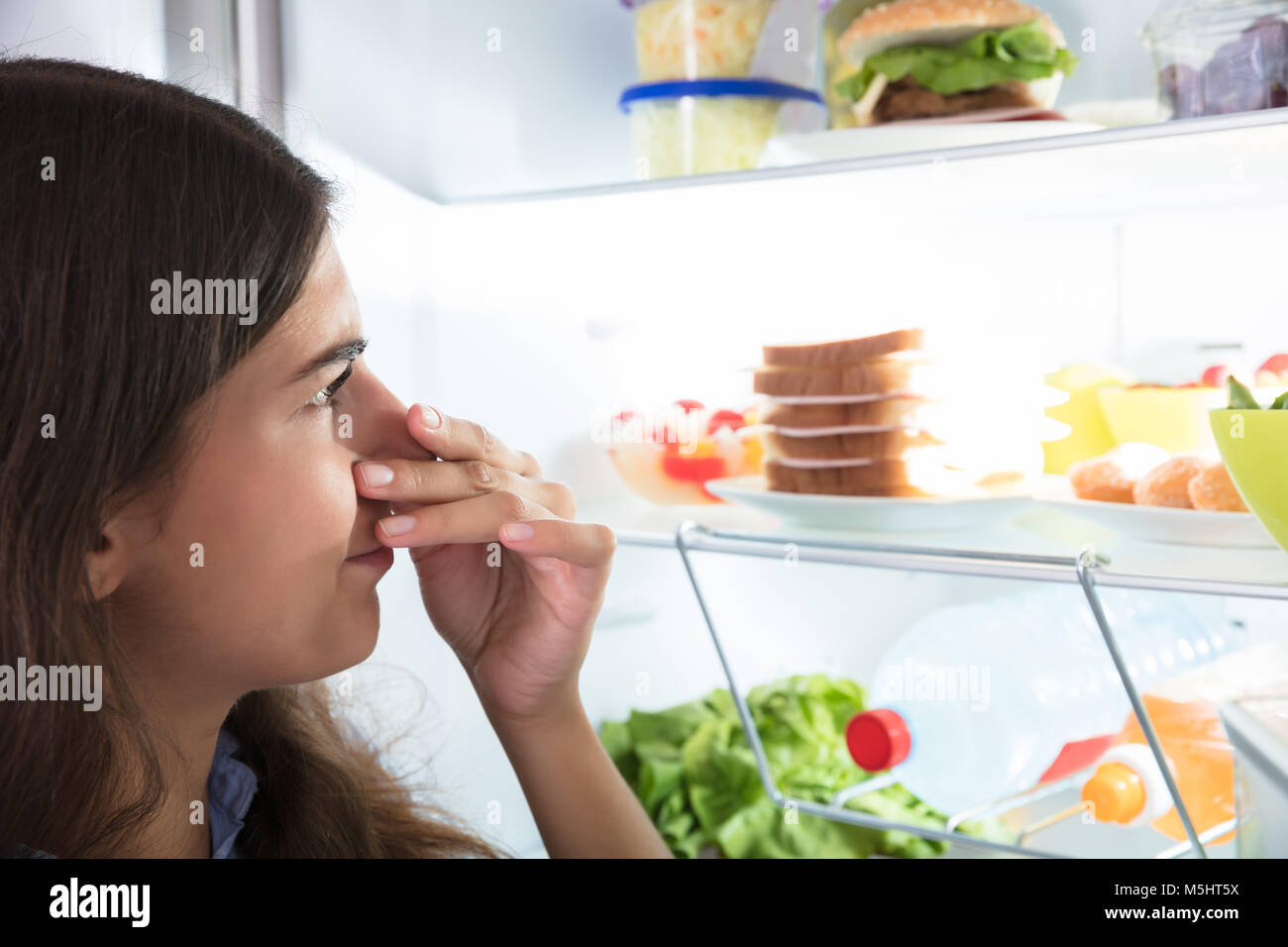 Close-up of a Young Woman Holding Her Nose près de mauvais aliments dans réfrigérateur Banque D'Images