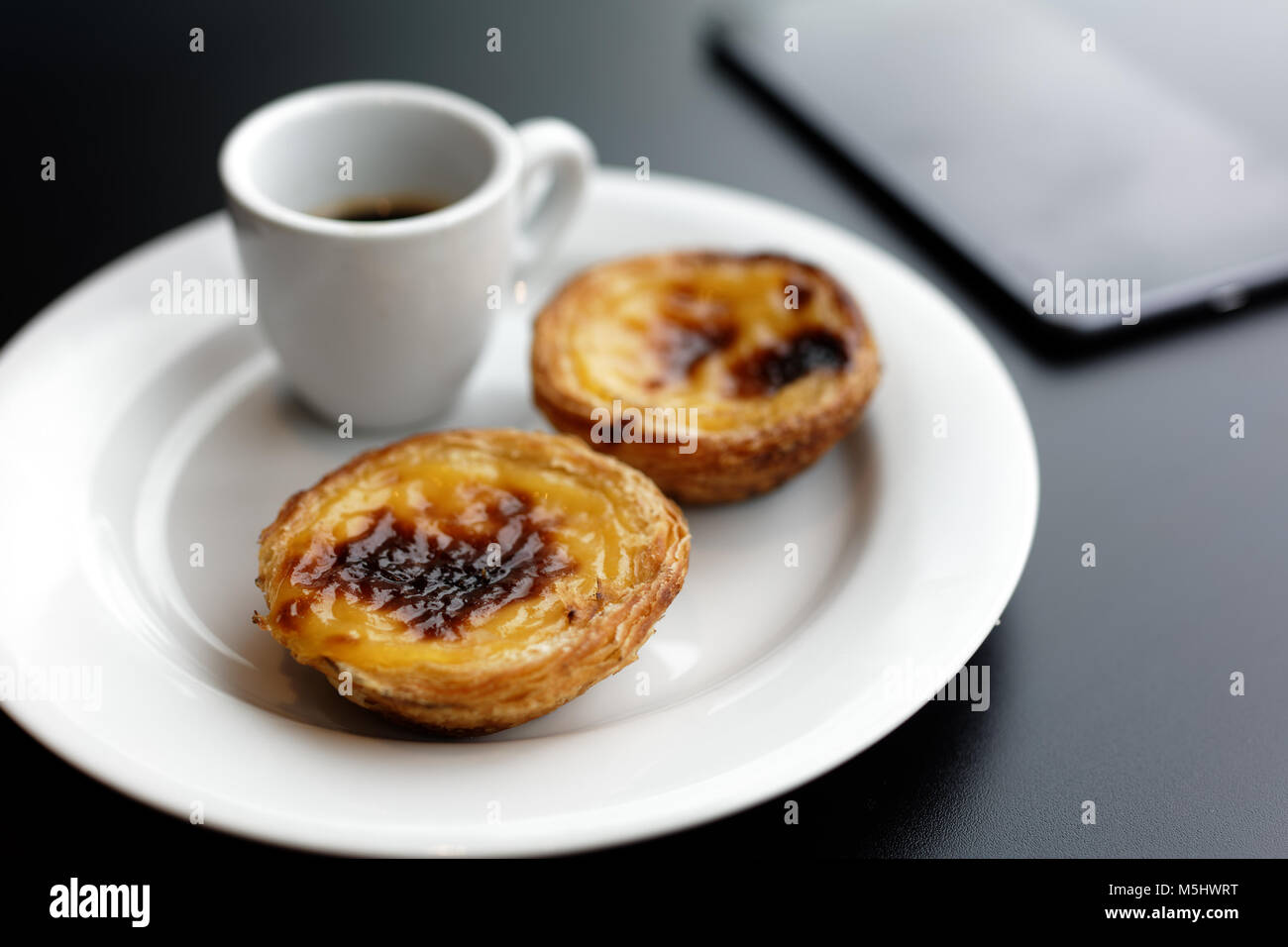 Tarte feuilletée oeuf portugais pastel de nata sur une plaque avec une tasse de café noir Banque D'Images