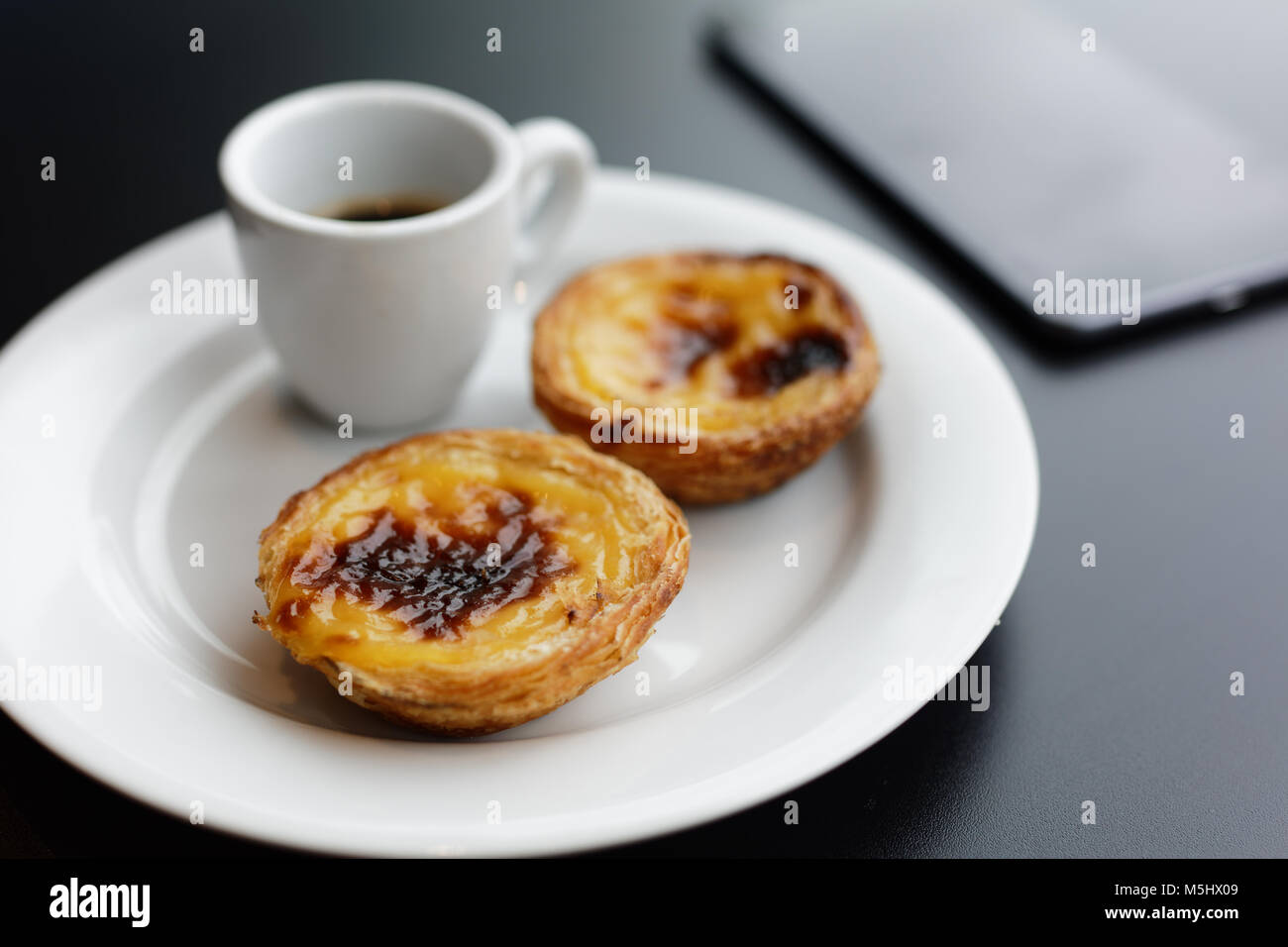 Tarte feuilletée oeuf portugais pastel de nata sur une plaque avec une tasse de café noir Banque D'Images