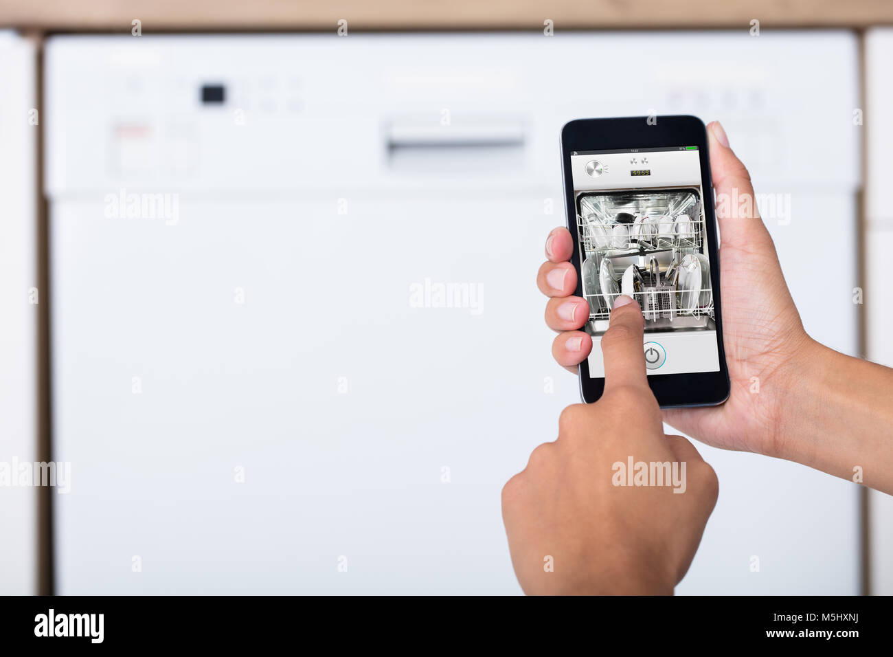 Close-up of Woman's Hand montrant lave-vaisselle App On Mobile Phone In Kitchen Banque D'Images