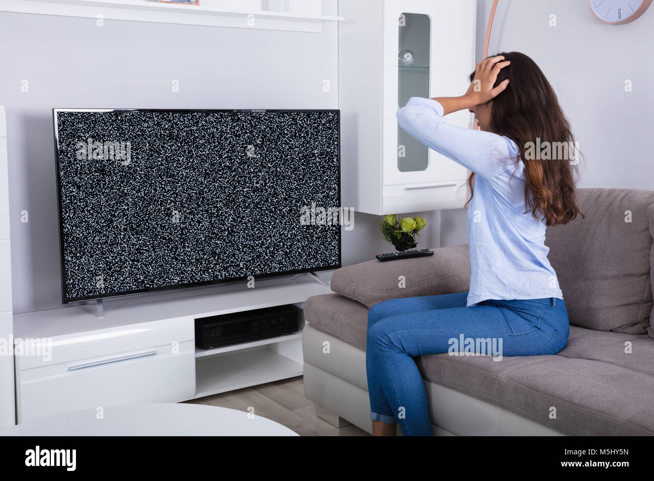 Vue arrière d'une femme sur canapé obtenir frustré avec Glitch écran de télévision à la maison Banque D'Images