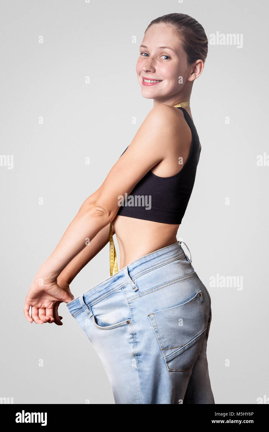Close-up de taille fine de jeune femme en gros jeans montrant la perte réussie de poids, isolé sur fond gris clair, le régime alimentaire concept. Banque D'Images