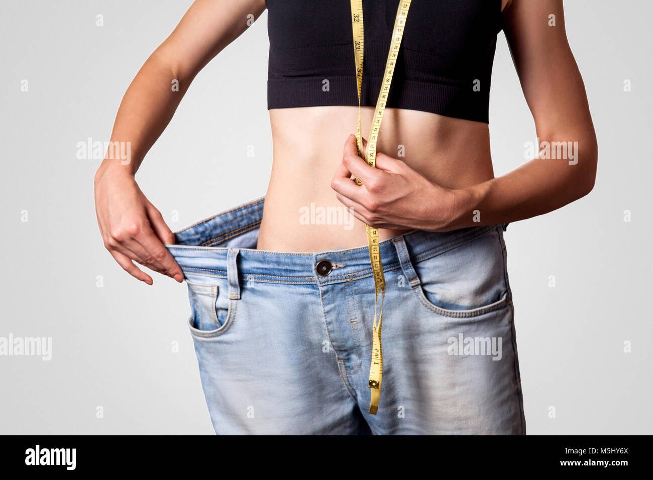Close-up de taille fine de jeune femme en gros jeans montrant la perte réussie de poids, isolé sur fond gris clair, le régime alimentaire concept. Banque D'Images