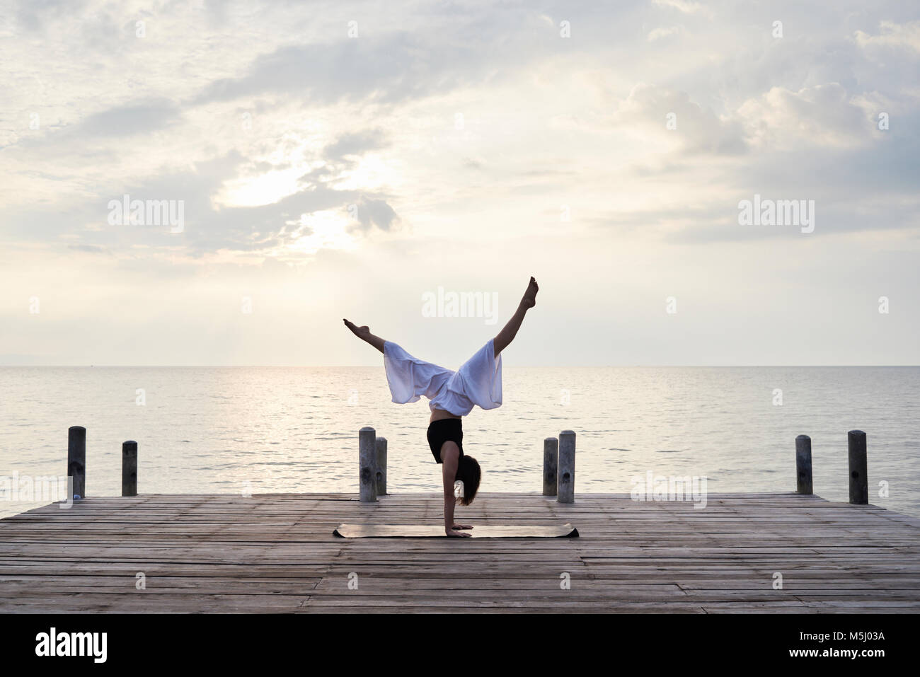 Professeur de Yoga debout à l'envers sur les mains tout en faisant du yoga contre le coucher du soleil et de la mer. Kep, au Cambodge. Banque D'Images