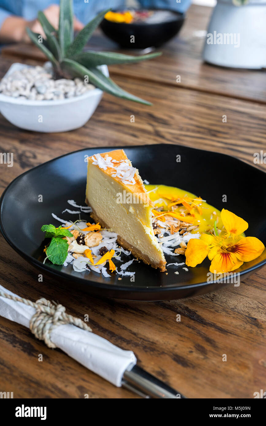 Morceau de gâteau au fromage avec des fleurs décorées sur table en bois Banque D'Images