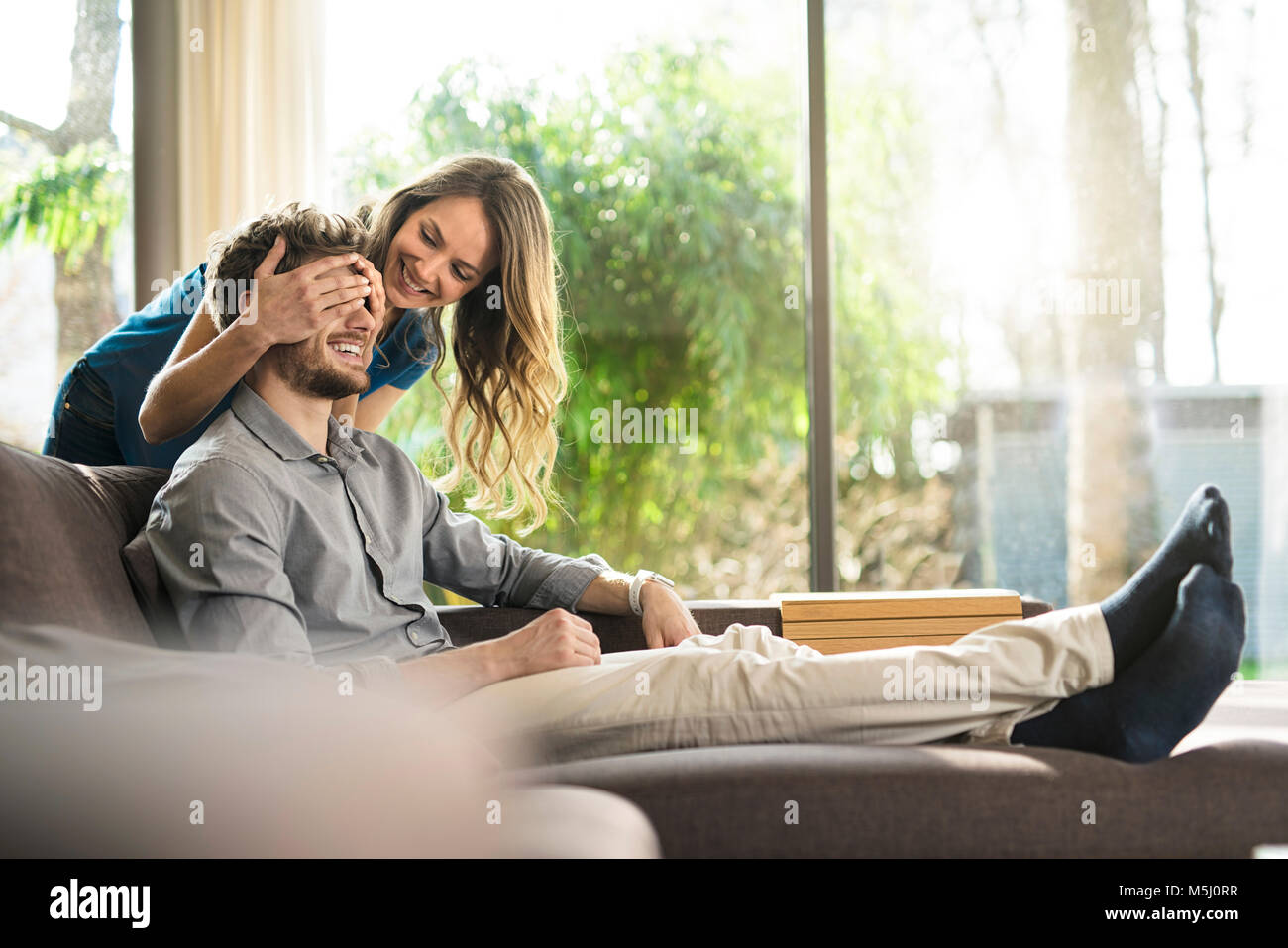 Smiling woman couvrant les yeux de son petit ami sur le canapé à la maison Banque D'Images