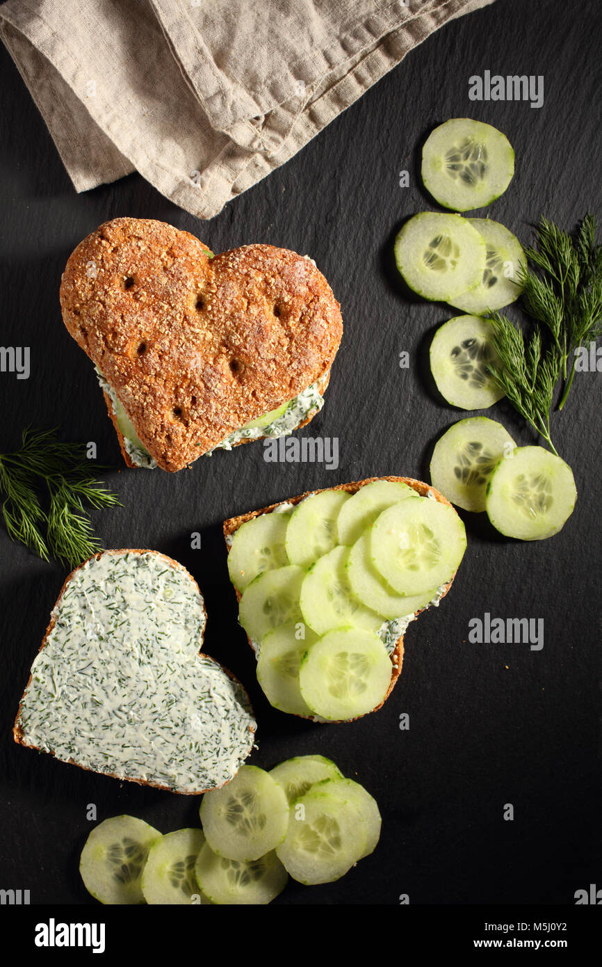 Deux sandwiches en forme de coeur avec le fromage à la crème, l'aneth et des tranches de concombre sur une liste de sélection Banque D'Images