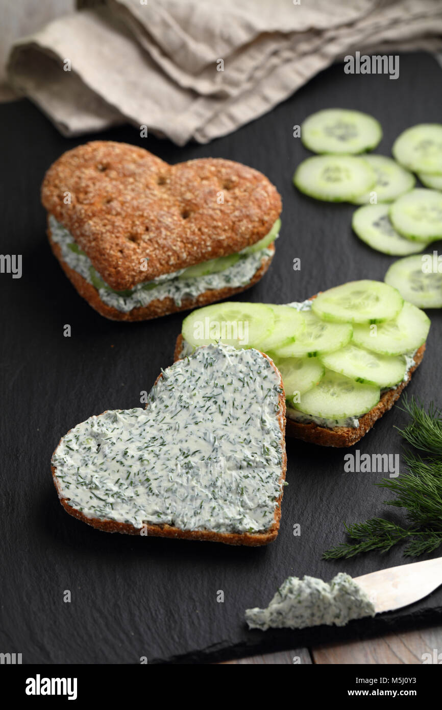 Deux sandwiches en forme de coeur avec le fromage à la crème, l'aneth et des tranches de concombre sur une liste de sélection Banque D'Images