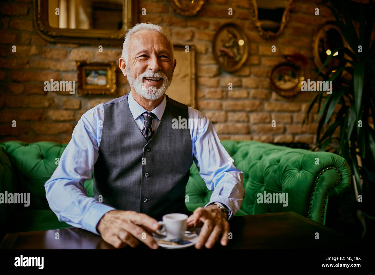 Portrait d'élégante senior man sitting on couch in a cafe smiling Banque D'Images