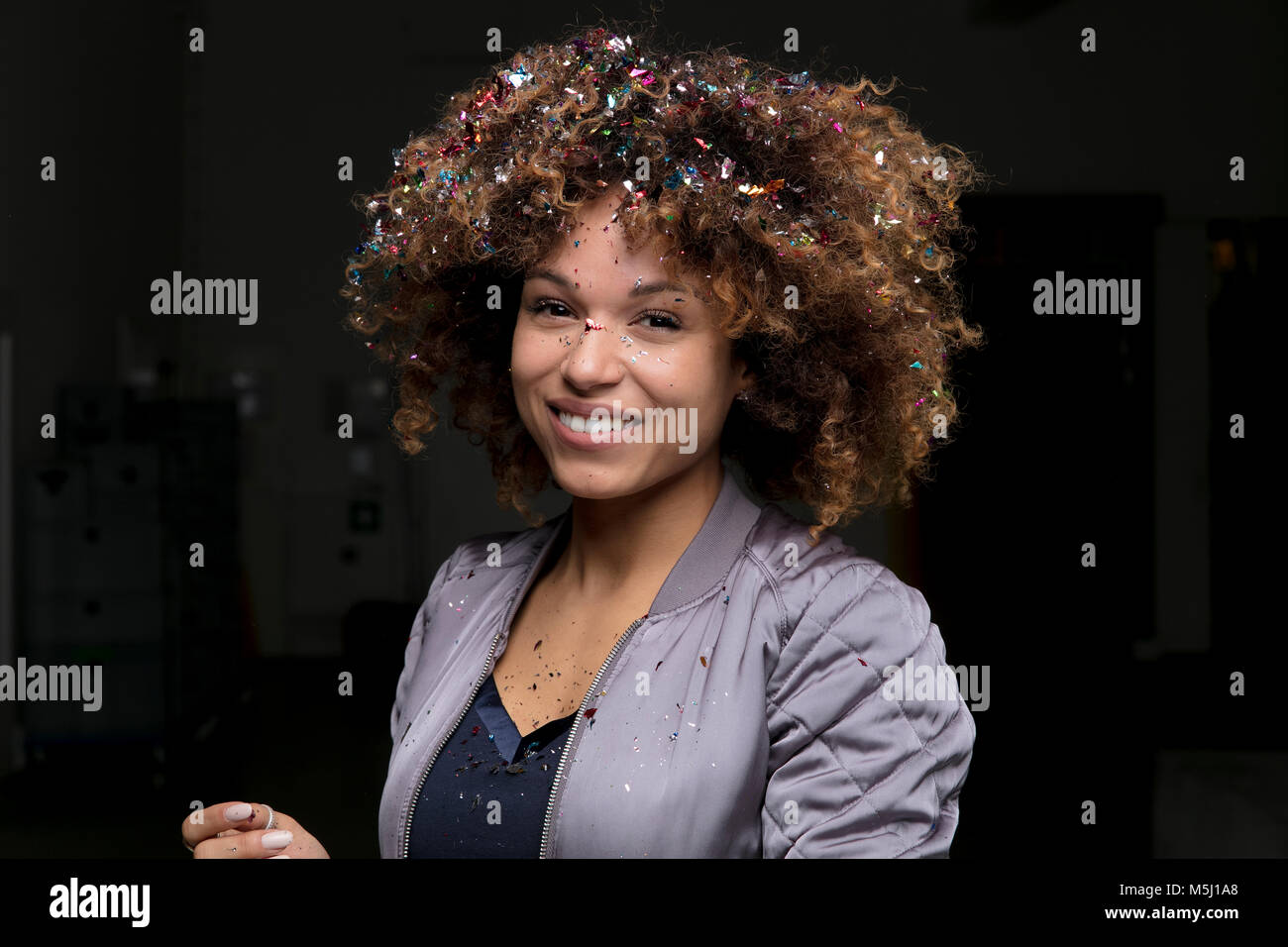 Portrait of laughing woman with confetti sur ses cheveux sur un fond sombre Banque D'Images Portrait of laughing woman with confetti sur ses cheveux sur un fond sombre Banque D'Images