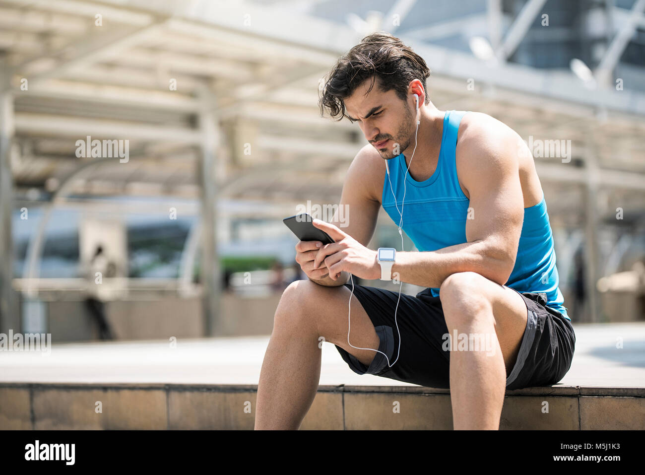 Runner wearing earphones, consultation des messages sur son smartphone Banque D'Images