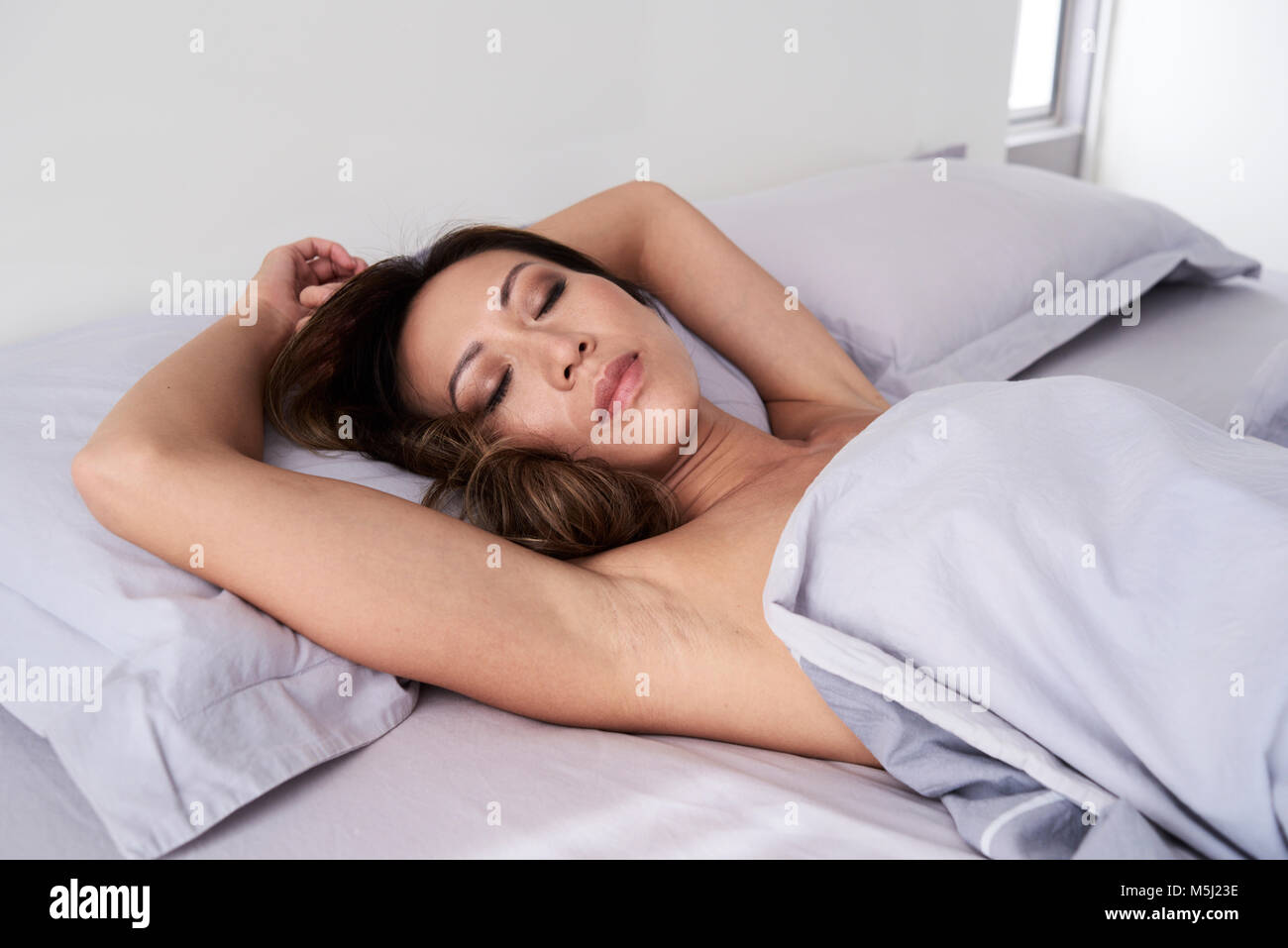 Jolie femme asiatique en couchage double dans appartement moderne sans pyjama. Banque D'Images