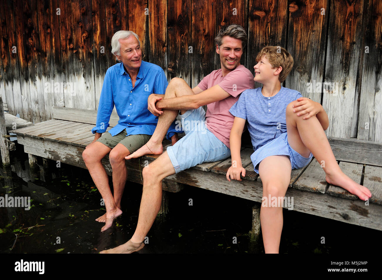 Garçon assis avec grand-père et père de concert sur jetty en été Banque D'Images