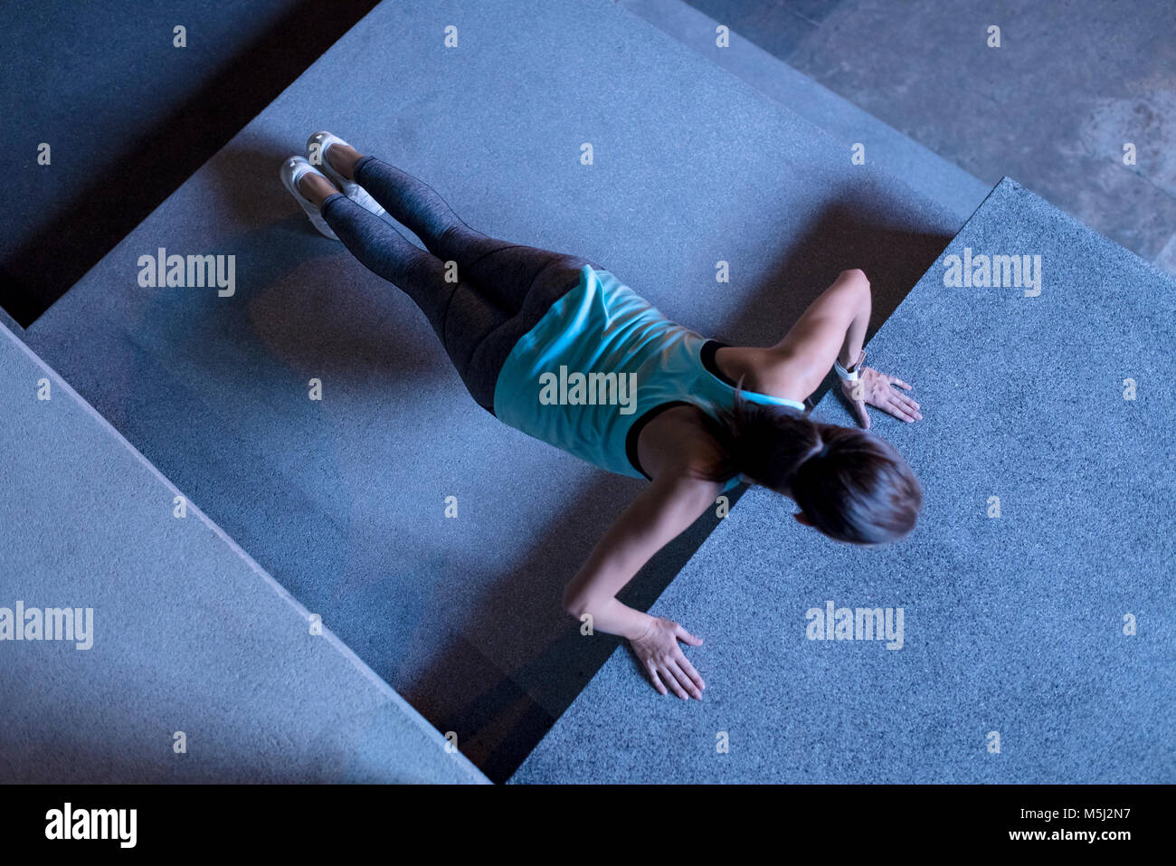 Young woman doing pushups en milieu urbain moderne dans la nuit Banque D'Images