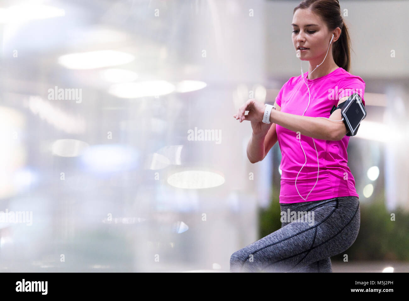 Jeune femme en rose sportshirt écouter de la musique et contrôle sa smartwatch en milieu urbain moderne Banque D'Images