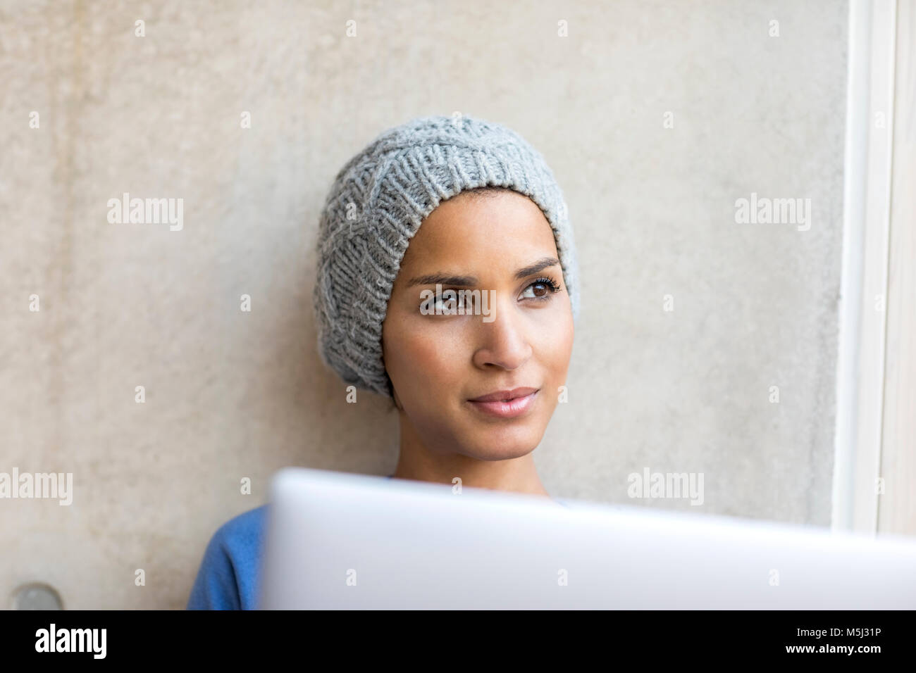 Portrait of smiling young woman with laptop à la fenêtre de Banque D'Images