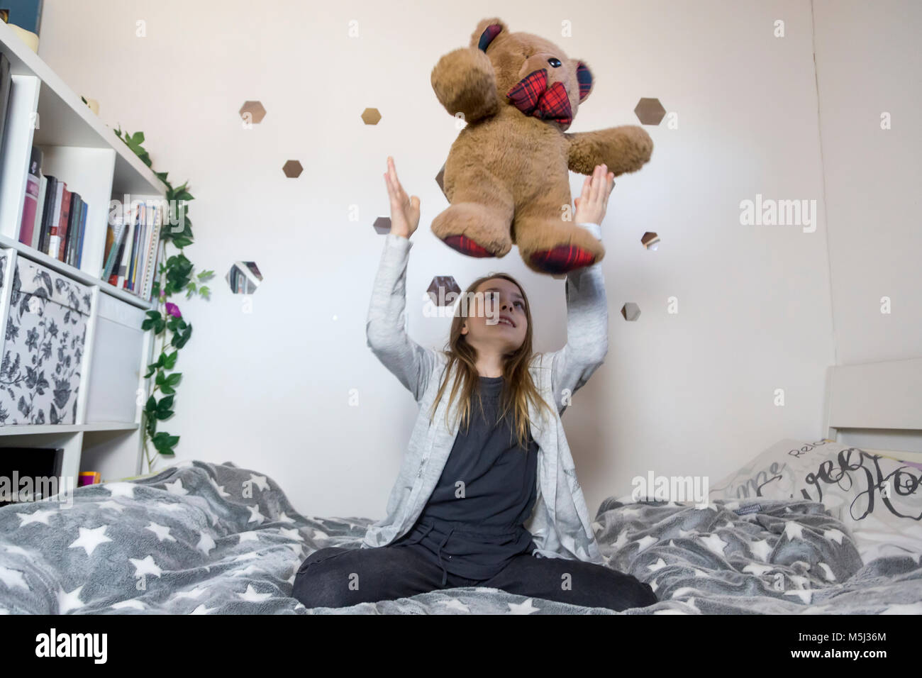 Smiling girl on bed jouer avec teddy bear Banque D'Images