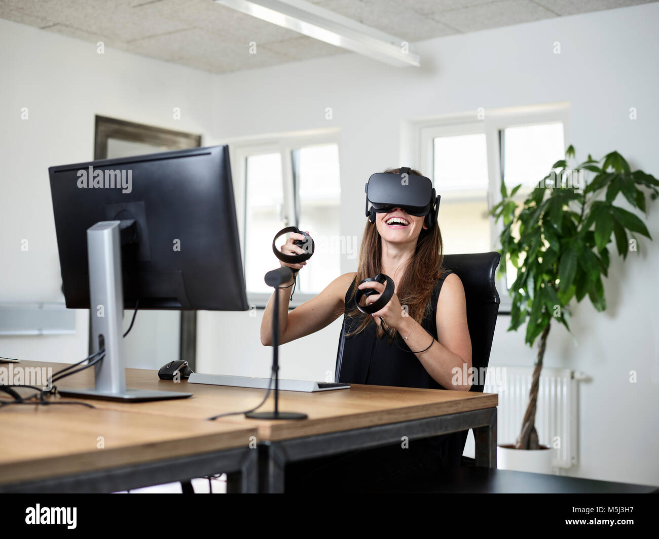 Happy woman lunettes VR at desk in office Banque D'Images