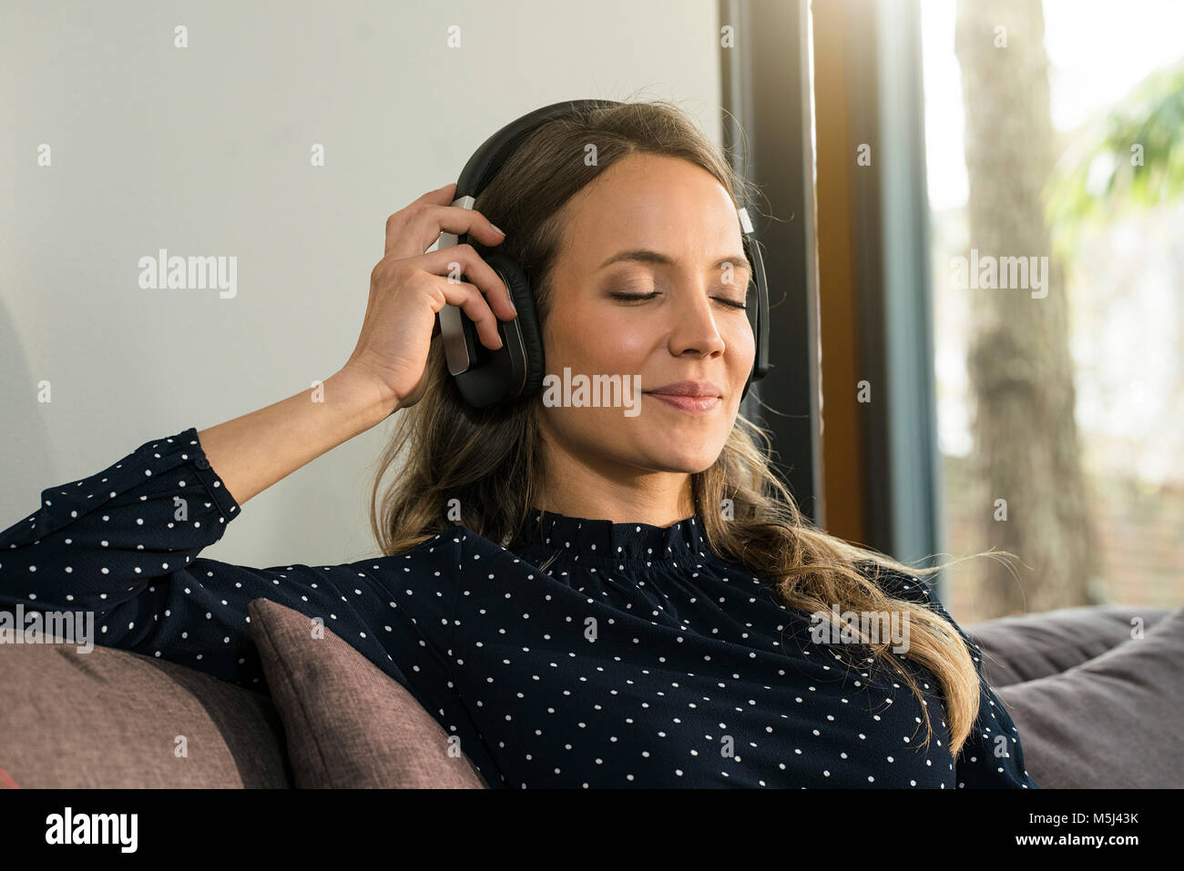 Portrait of smiling woman with headphones relaxing at home Banque D'Images