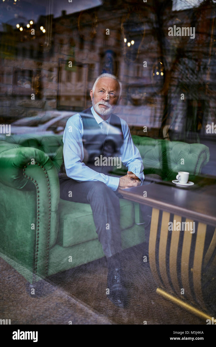 Élégant senior man sitting on couch in a cafe à la fenêtre de Banque D'Images