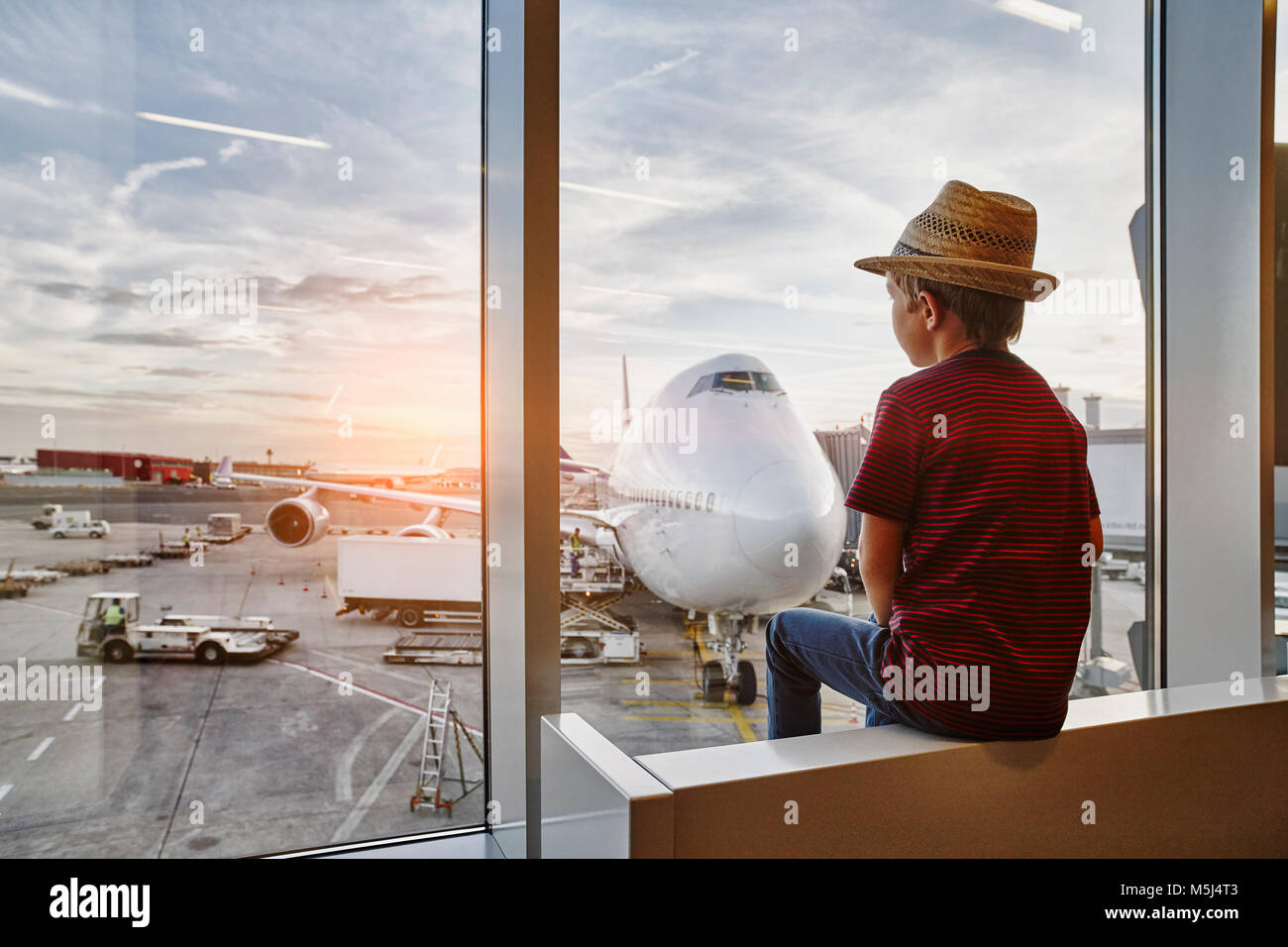 Boy wearing straw hat à la recherche d'une fenêtre d'avion sur le tarmac Banque D'Images