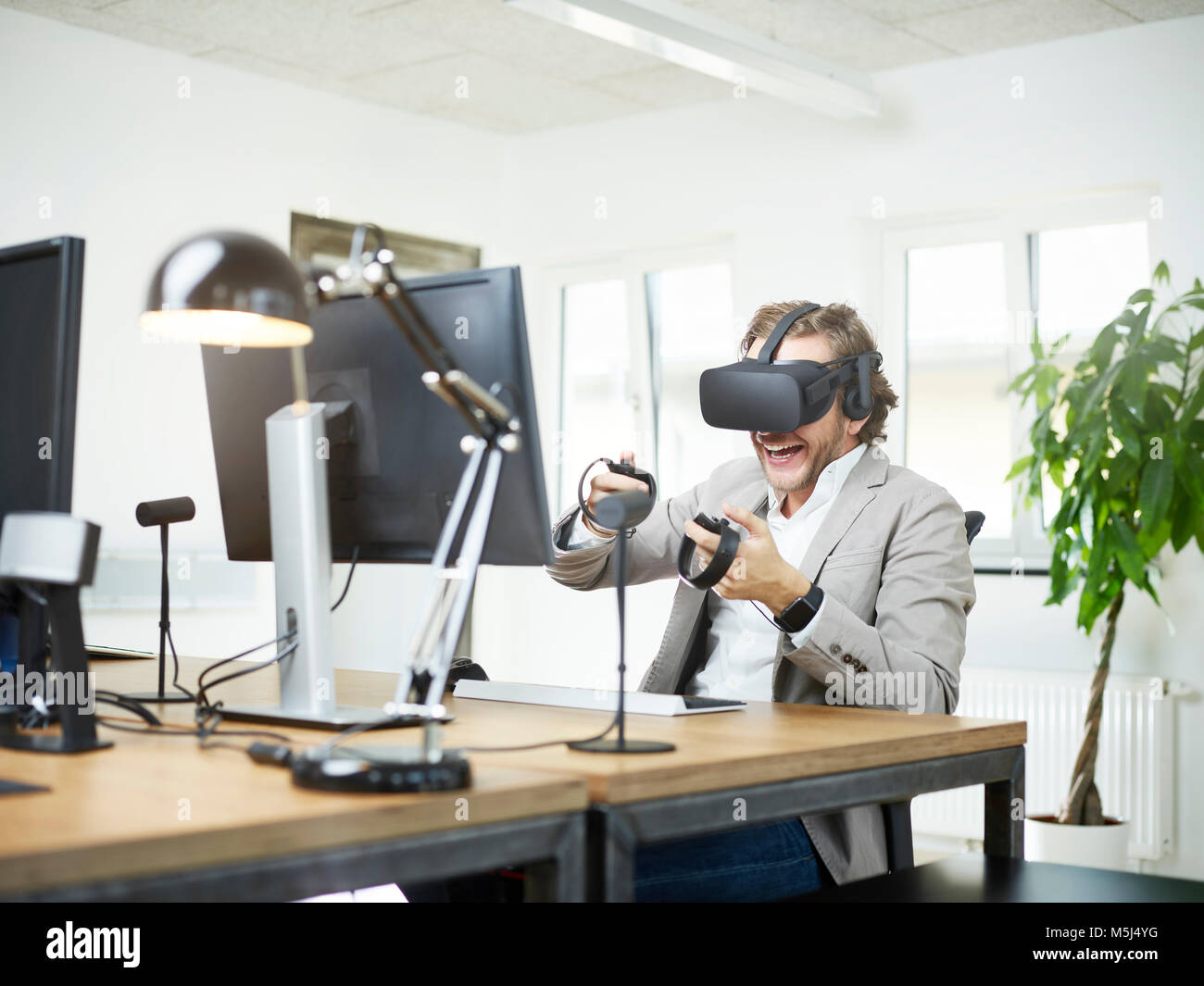 Heureux homme portant lunettes VR at desk in office Banque D'Images