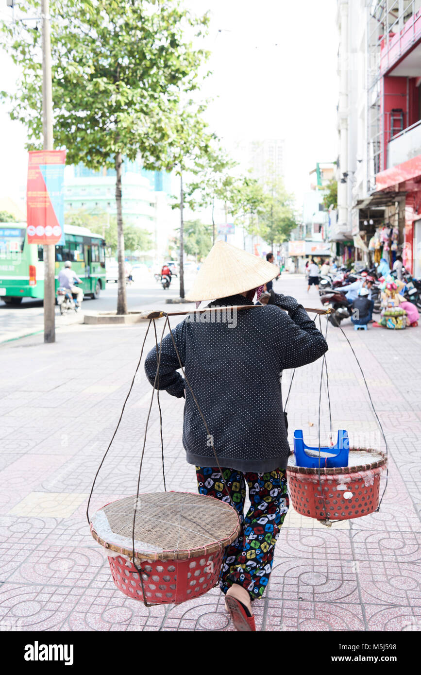 Vendeur de rue typique avec chapeau vietnamien transportant des marchandises le long de à Ho Chi Minh, Vietnam. Banque D'Images