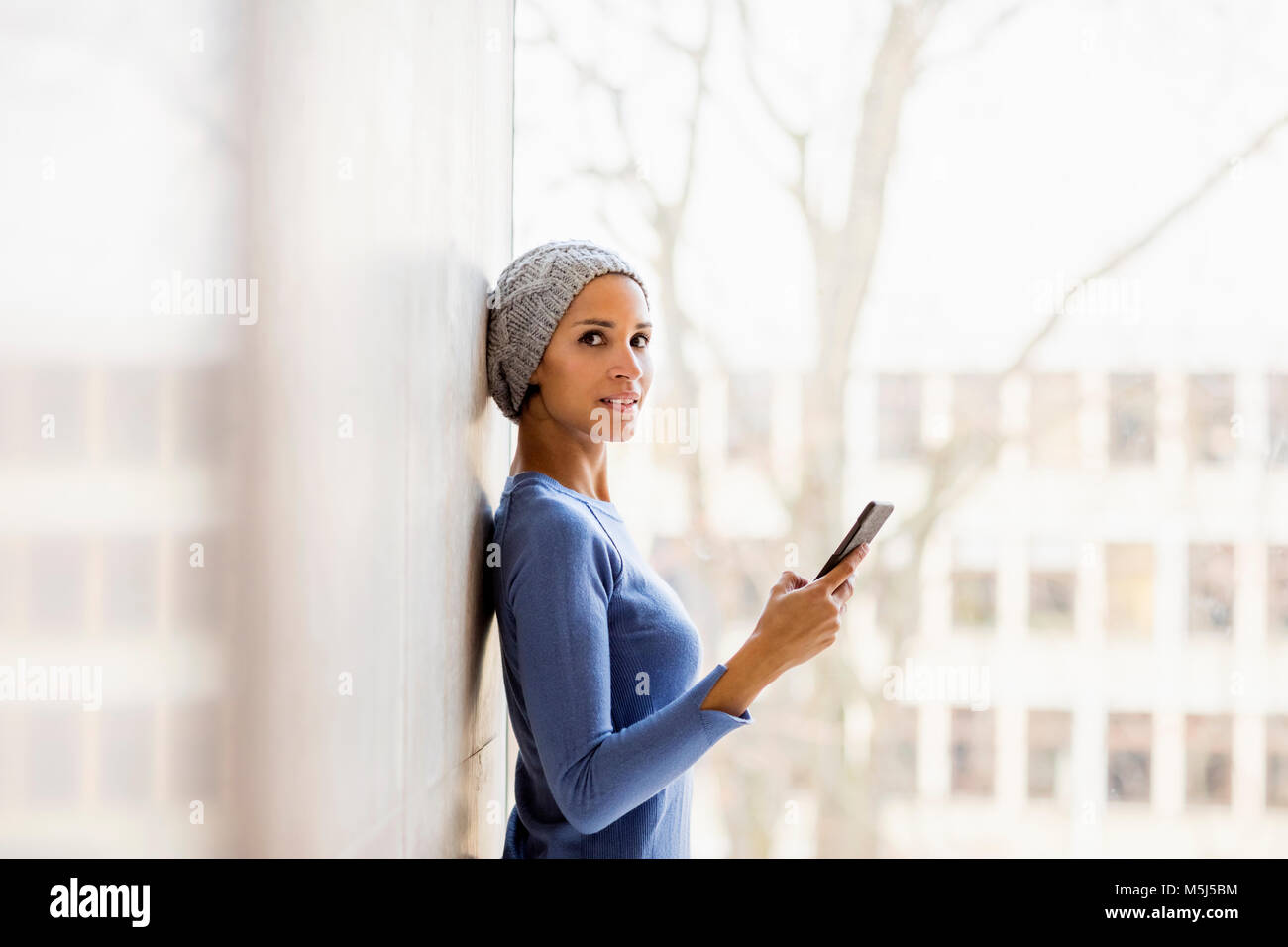 Portrait of young woman with cell phone in front of window Banque D'Images