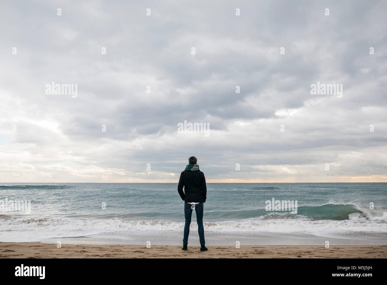 Vue arrière de l'homme debout sur la plage en hiver à la recherche à distance Banque D'Images