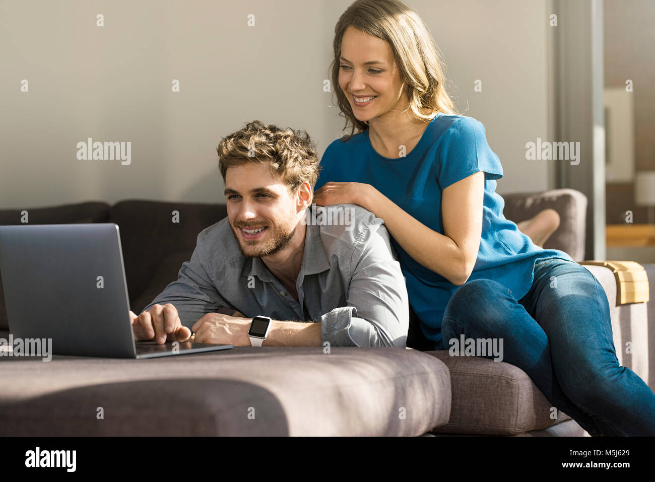 Smiling couple using laptop on sofa at home Banque D'Images