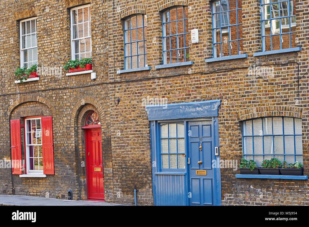 Une jolie ligne de brique maison mitoyenne avec le rouge et le bleu des portes, des volets rouges à une fenêtre et les jardinières à Southwark London Banque D'Images
