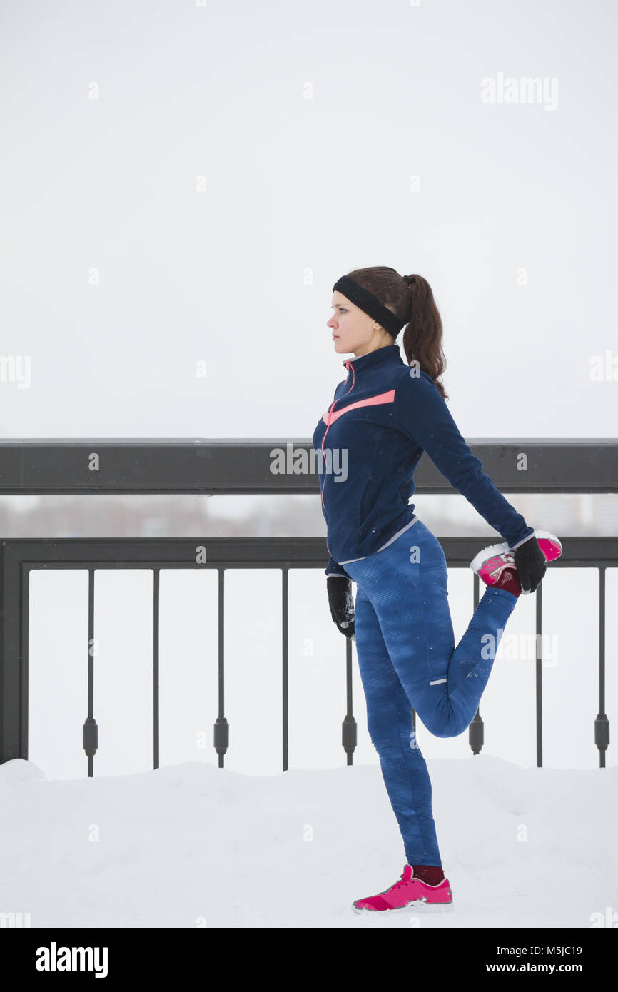 Coureuse faisant de l'exercice de souplesse pour les jambes avant de courir à neige hiver promenade, vertical Banque D'Images