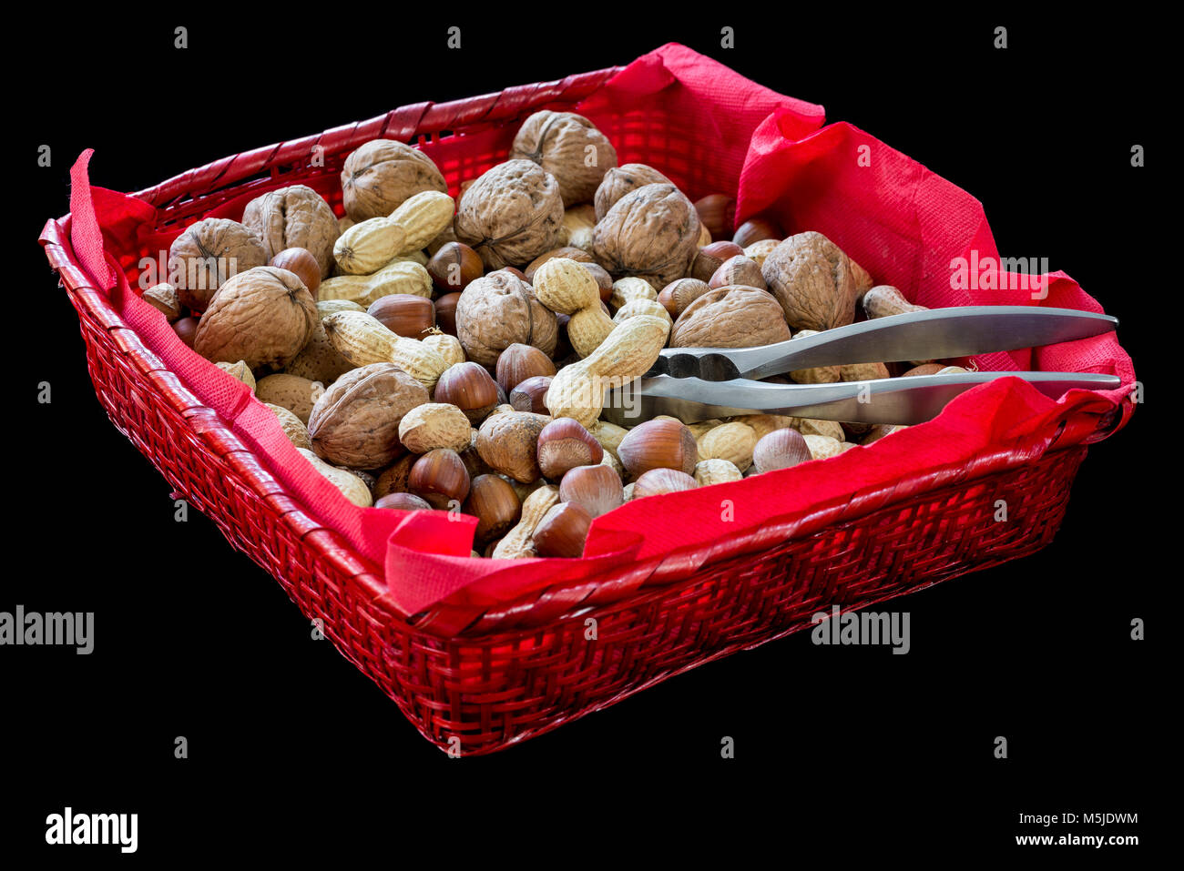 Panier en osier rouge avec des fruits secs, noisettes, noix, amandes, arachides et un casse-noix sur fond noir Banque D'Images