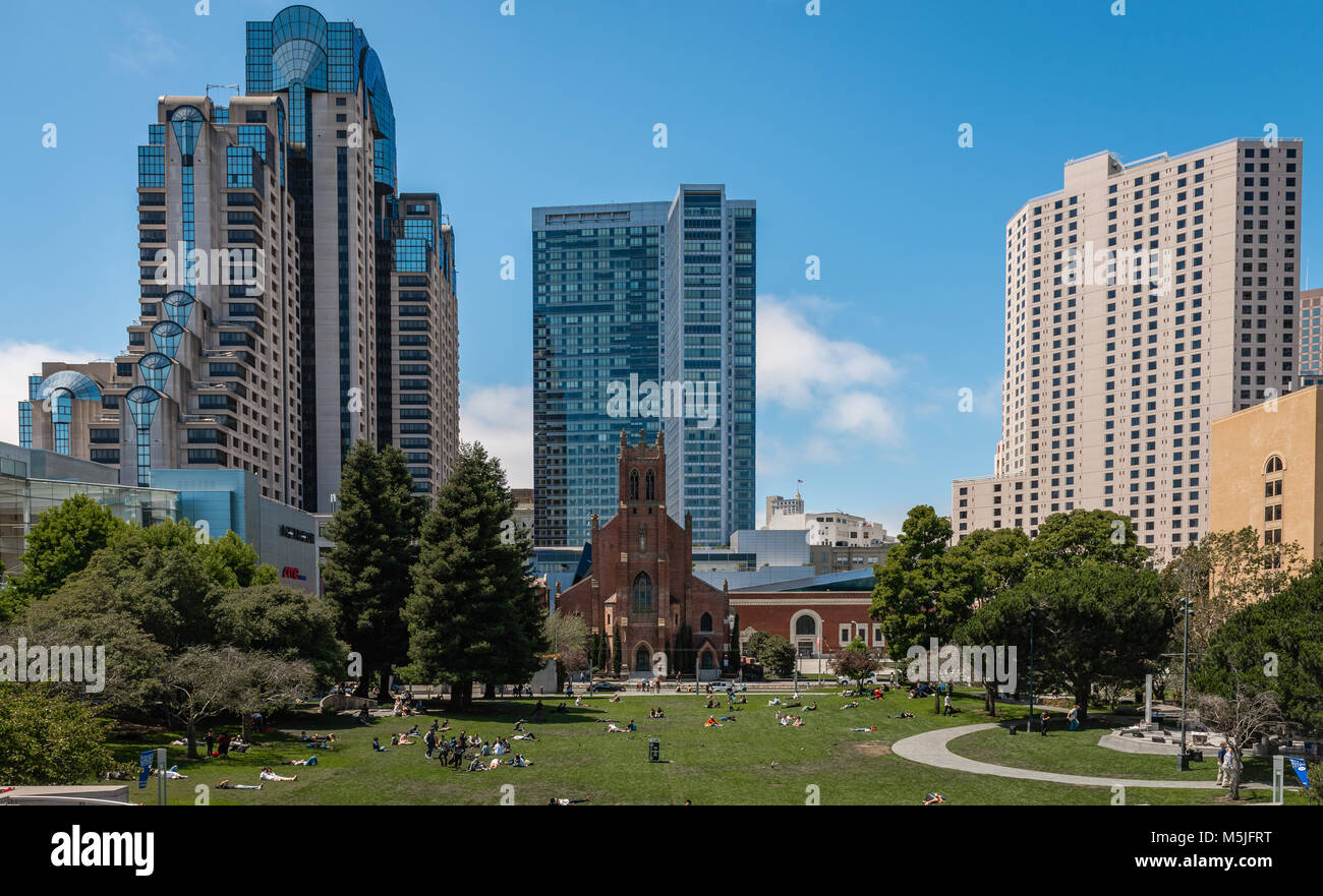 Les personnes bénéficiant de l'été soleil à Yerba Buena Gardens, San Francisco. L'église gothique St Patrick's se trouve sous l'ombre de l'édifices modernes. Banque D'Images