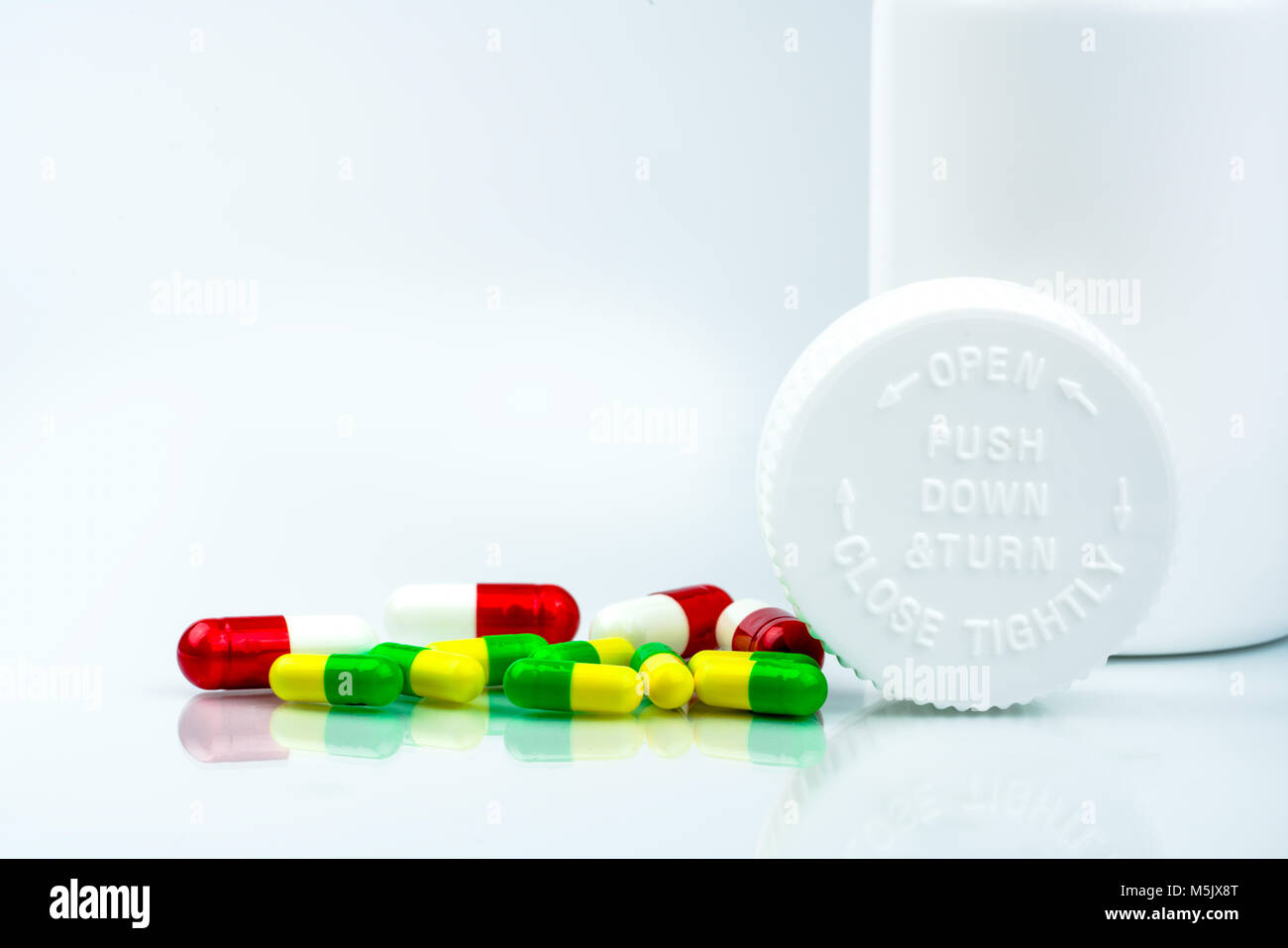 Pilules colorées sur fond blanc et en plastique bouteille avec étiquette vierge et copiez l'espace. Emballage sécurité enfant. Comprimé résistant aux enfants contenant. Pousser vers le bas Banque D'Images