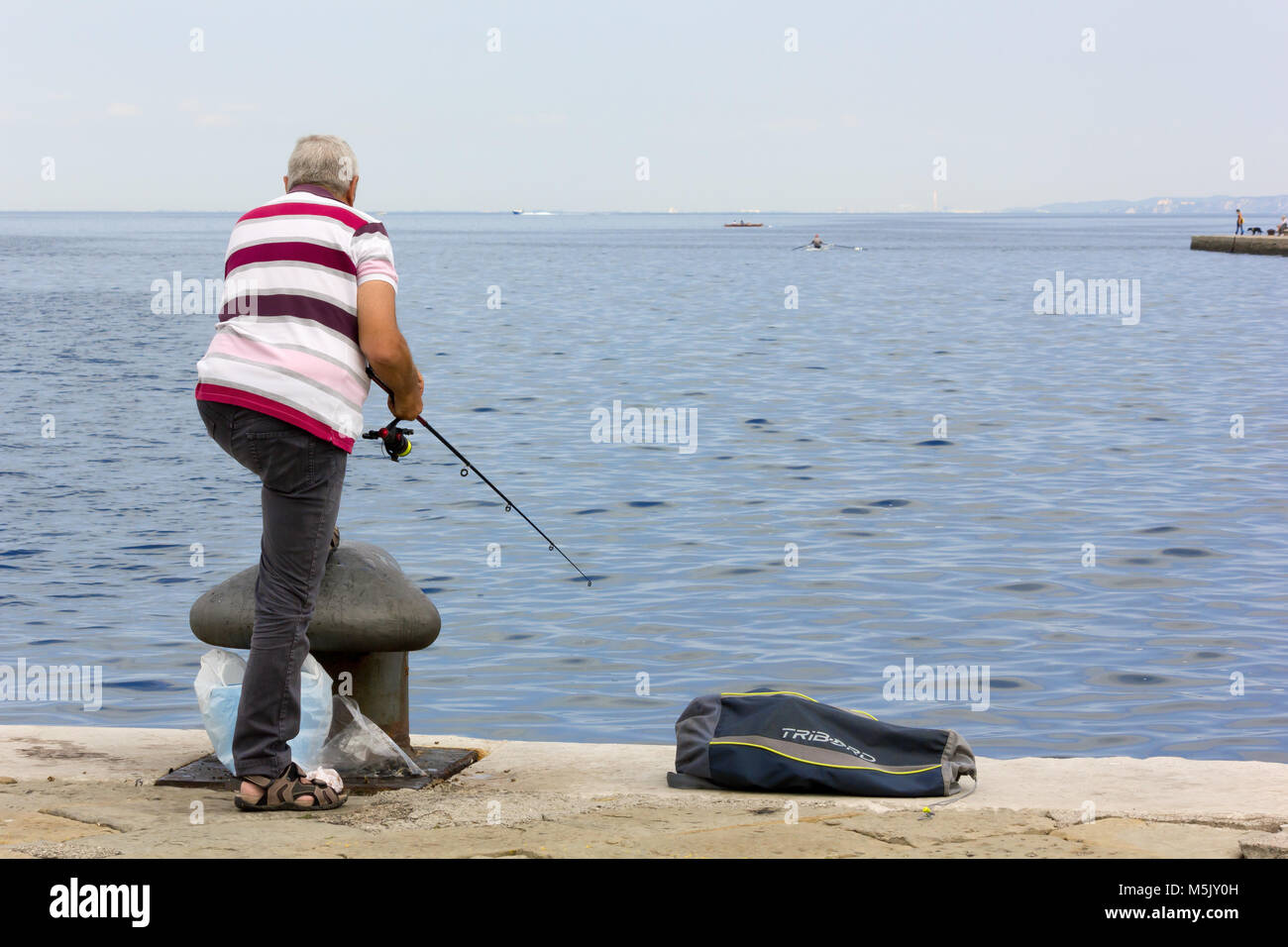 TRIESTE, Italie - 23 juin 2014 : l'homme vu de dos de la ville de pêche front de mer près d'une borne haute Banque D'Images