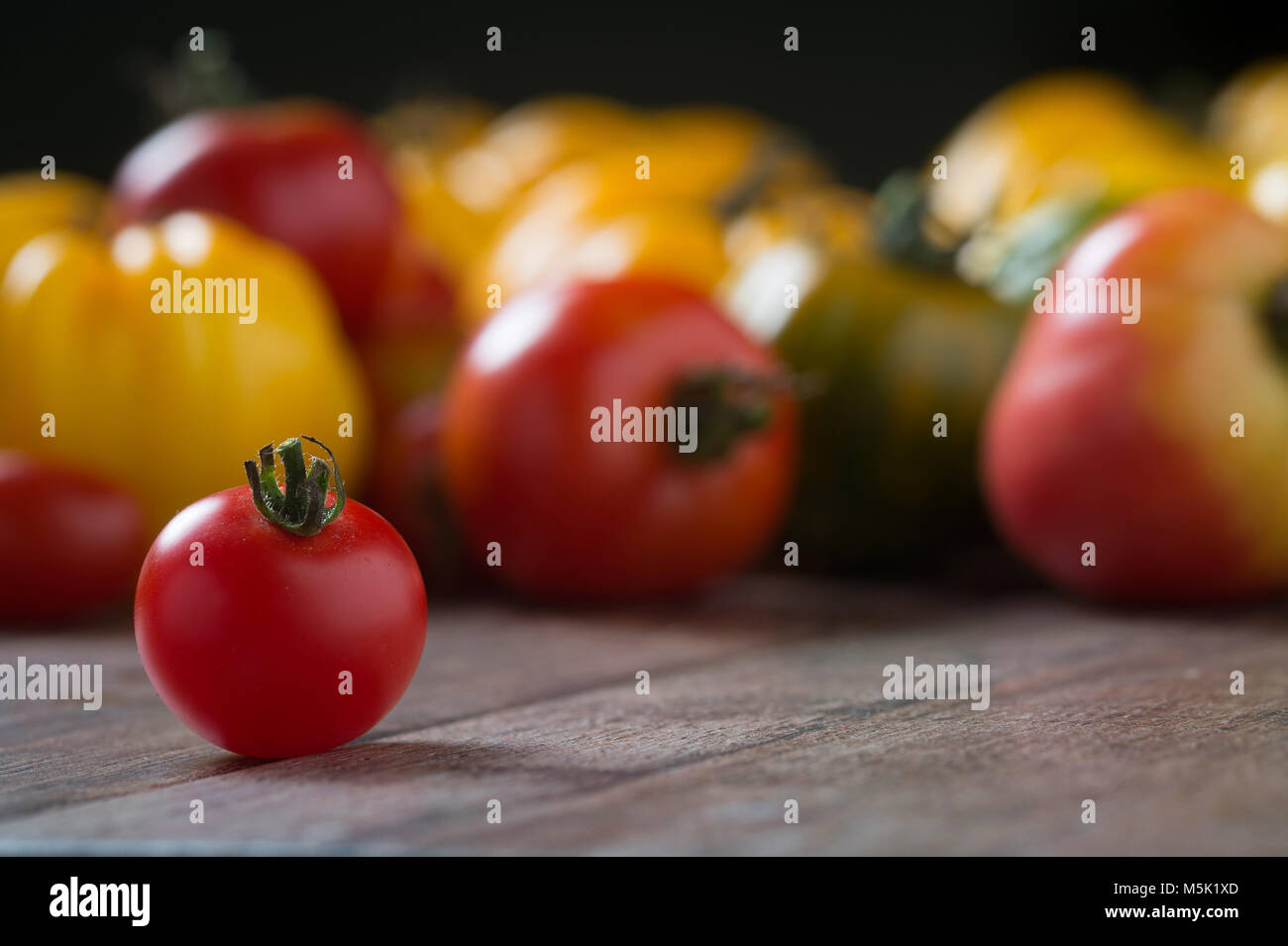 Tomate cerise sur fond en bois rustique avec des tomates en contexte. Profondeur de champ. Banque D'Images