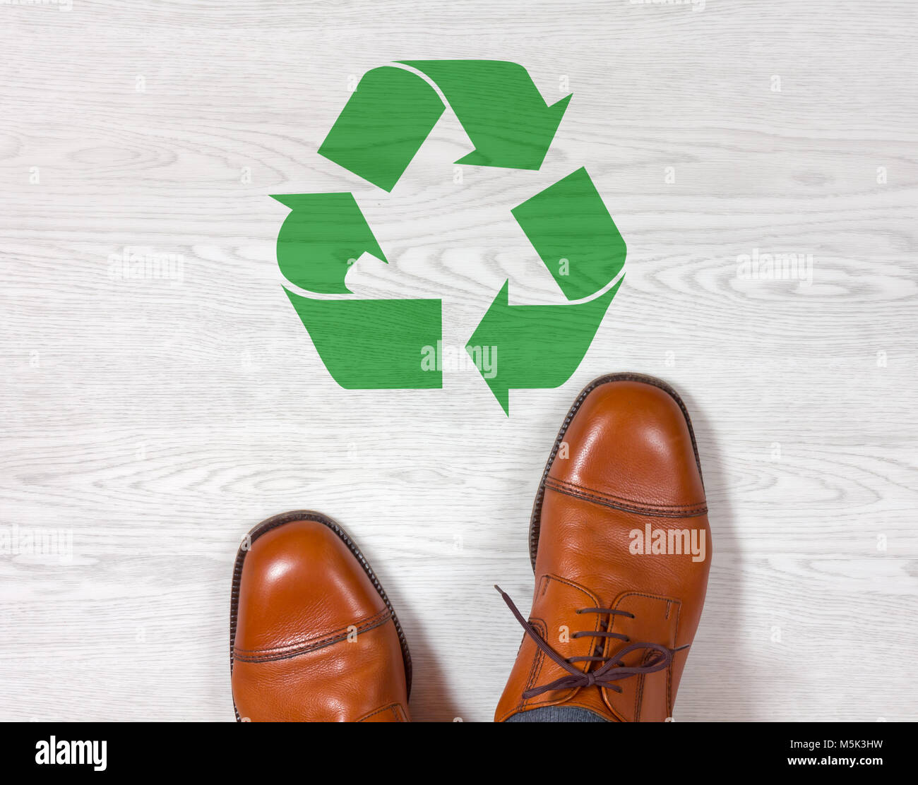 Chaussures homme classique élégant debout sur un plancher en bois blanc avec un symbole de recyclage vert peint sur elle Banque D'Images