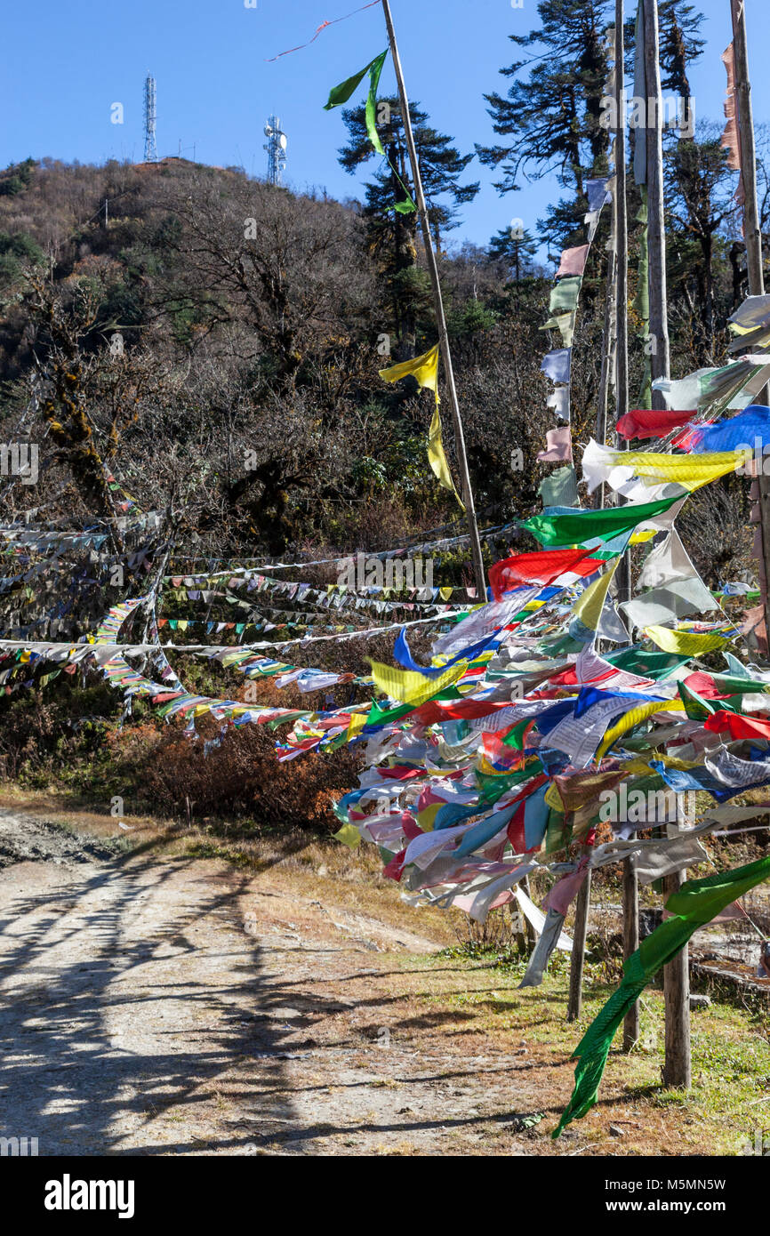 Trongsa, Bhoutan. Juxtaposition de méthodes de communication : drapeaux de prière céleste bouddhiste moderne par rapport au signal téléphonique tour de relais. Yotong Pass. Banque D'Images