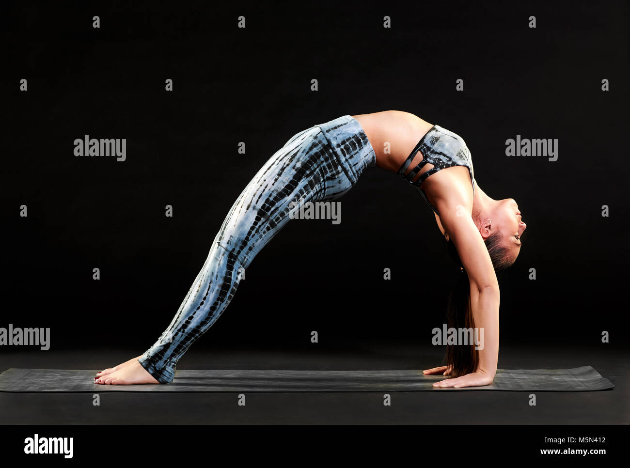 Fit la démonstration d'une femme athlétique pattes droites pose des roues pendant le yoga se cambrant avec pieds et mains sur le tapis dans une petite v Banque D'Images