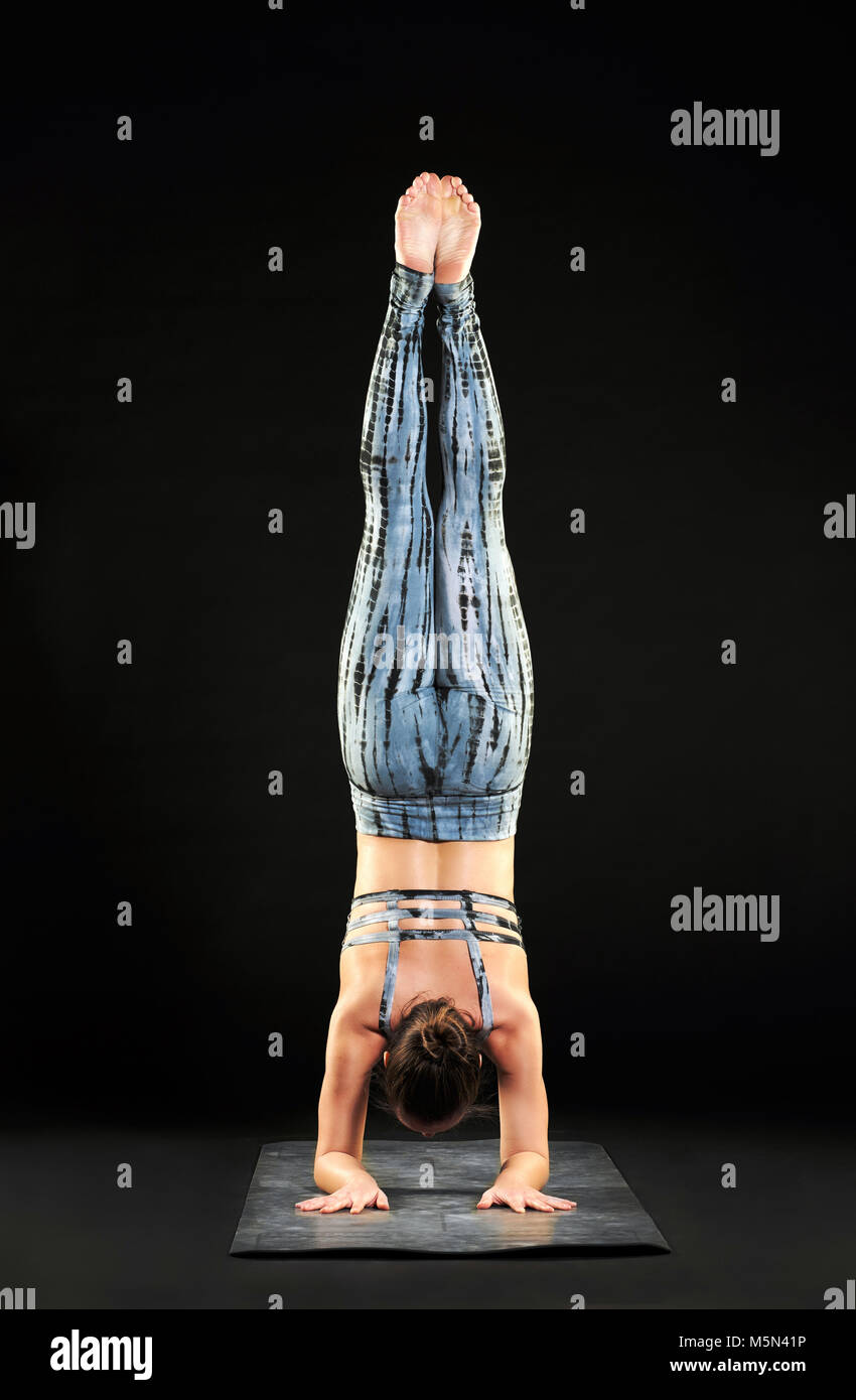 Femme musculaire démontrant un stand de l'avant-bras ou pincha poser dans le yoga comme elle travaille sur un mat sur un fond sombre en équilibre sur ses bras avec son bo Banque D'Images