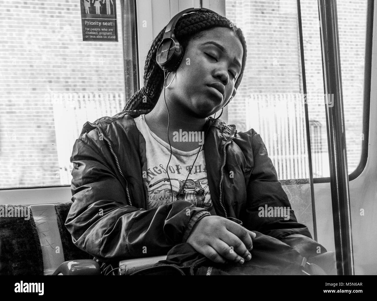 Noir et blanc / monochrome. Jeune femme noire somnoler passager sur London Underground tube train, écouter de la musique avec des écouteurs. Angleterre, Royaume-Uni. Banque D'Images