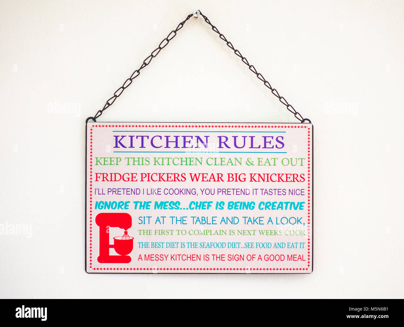 Liste des règles de cuisine amusante, imprimé sur un panneau oblong, suspendu par une chaîne sur un mur intérieur de la maison. Angleterre, Royaume-Uni. Banque D'Images