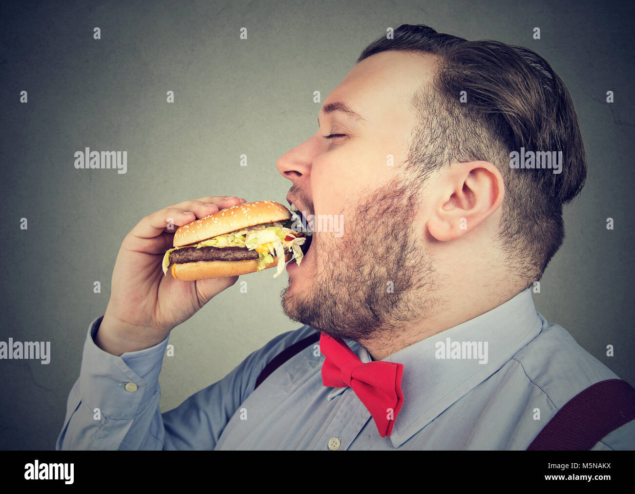 Profil de côté un gros homme mangeant un hamburger juteux Banque D'Images