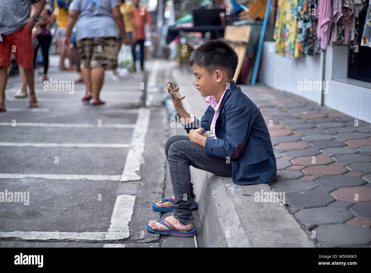 Enfant jouant seul dans la rue avec son smartphone. Thaïlande Asie du Sud-est Banque D'Images