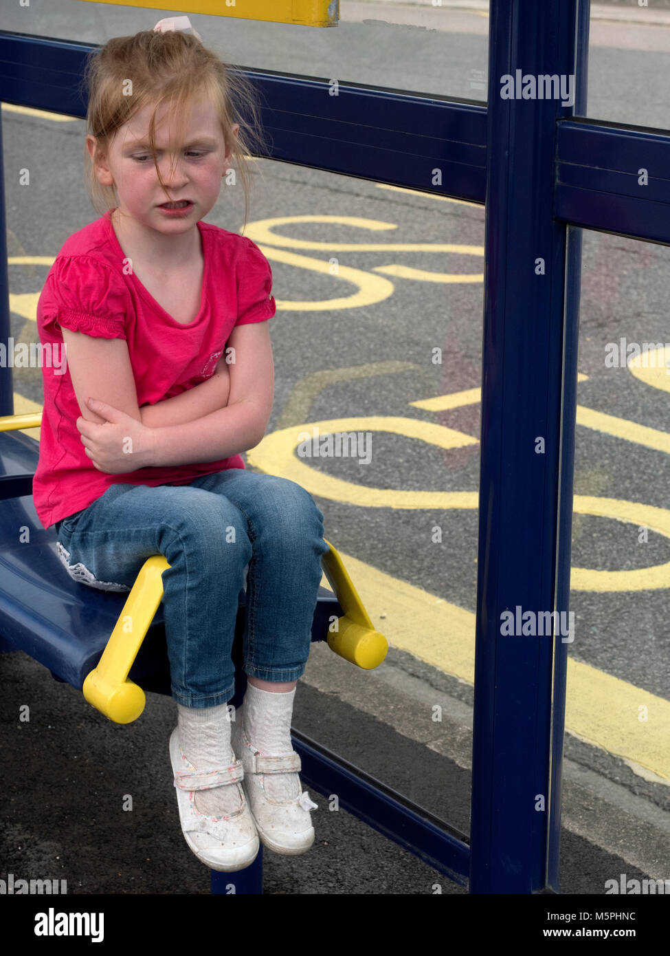 Jeune fille assise sur un siège d'abri de bus regardant la croix avec les bras pliés, Portsmouth, Hampshire, Angleterre, Royaume-Uni Banque D'Images