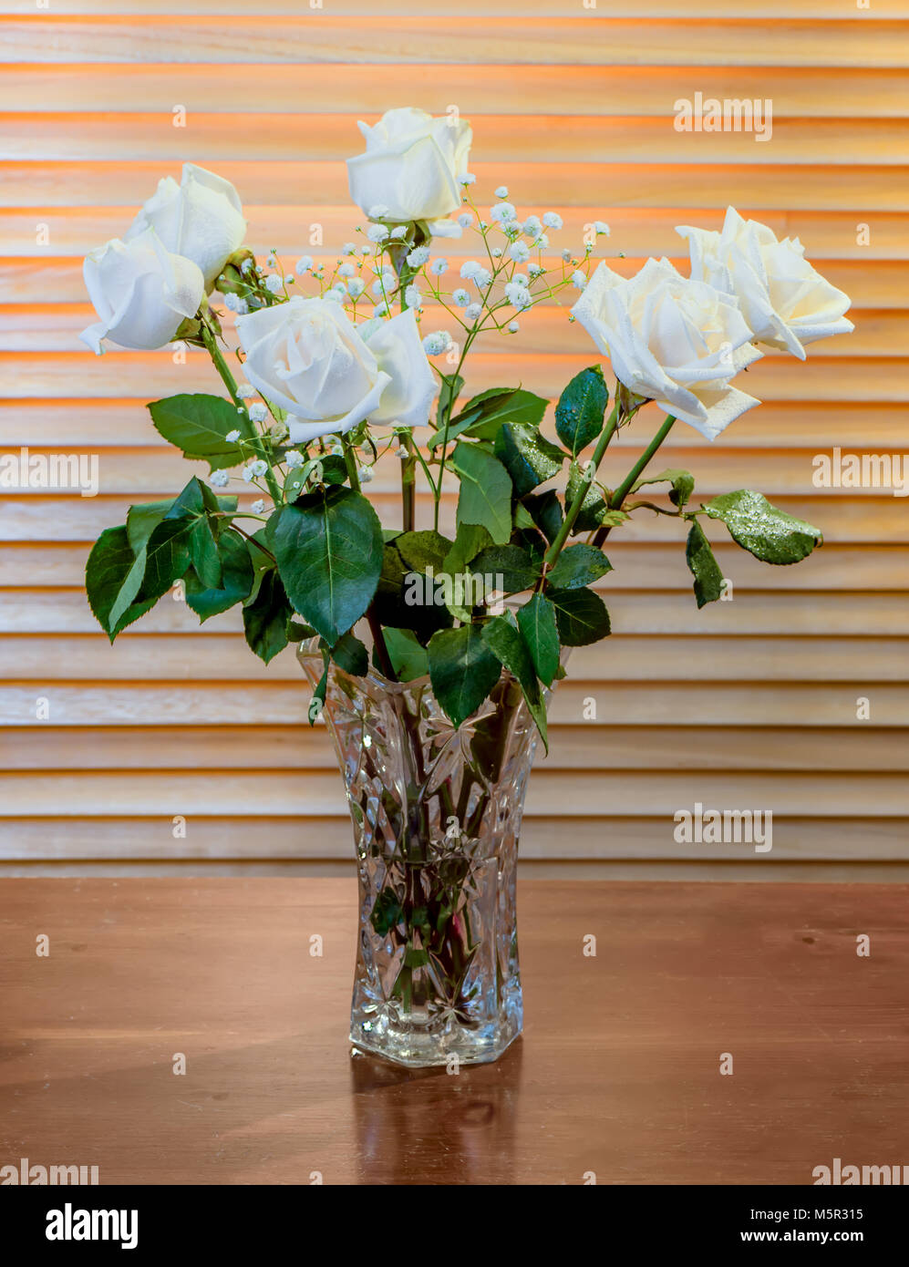L'usine est un bouquet de roses blanches avec des feuilles vertes et petites fleurs blanches, dans un vase en verre sur une table en bois brun foncé, dans le contexte d'ye Banque D'Images
