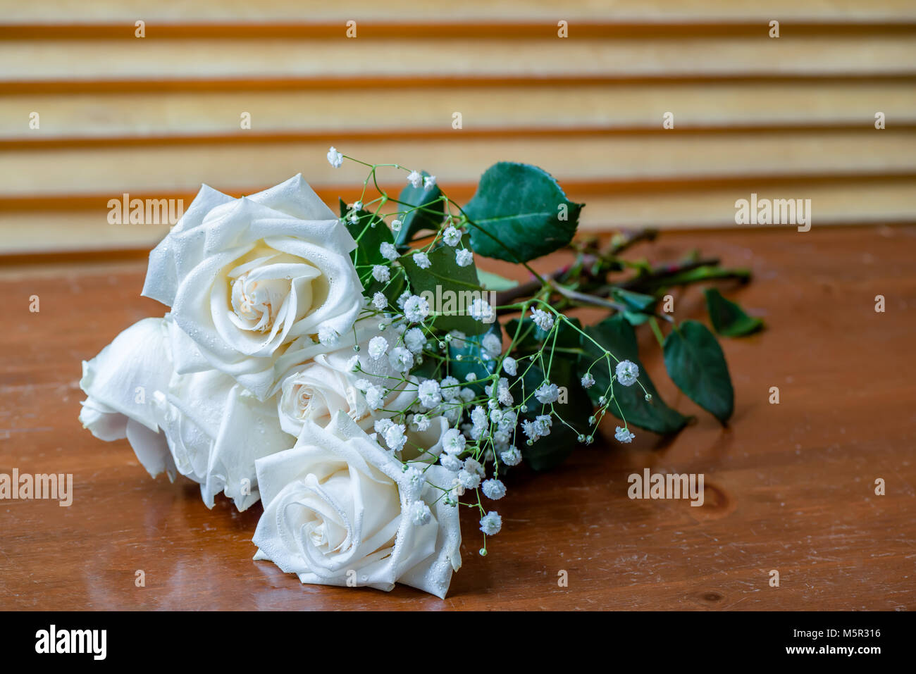 L\u0027usine est un bouquet de roses blanches avec des feuilles vertes et petites fleurs blanches, allongé sur une vieille table en bois, brown,