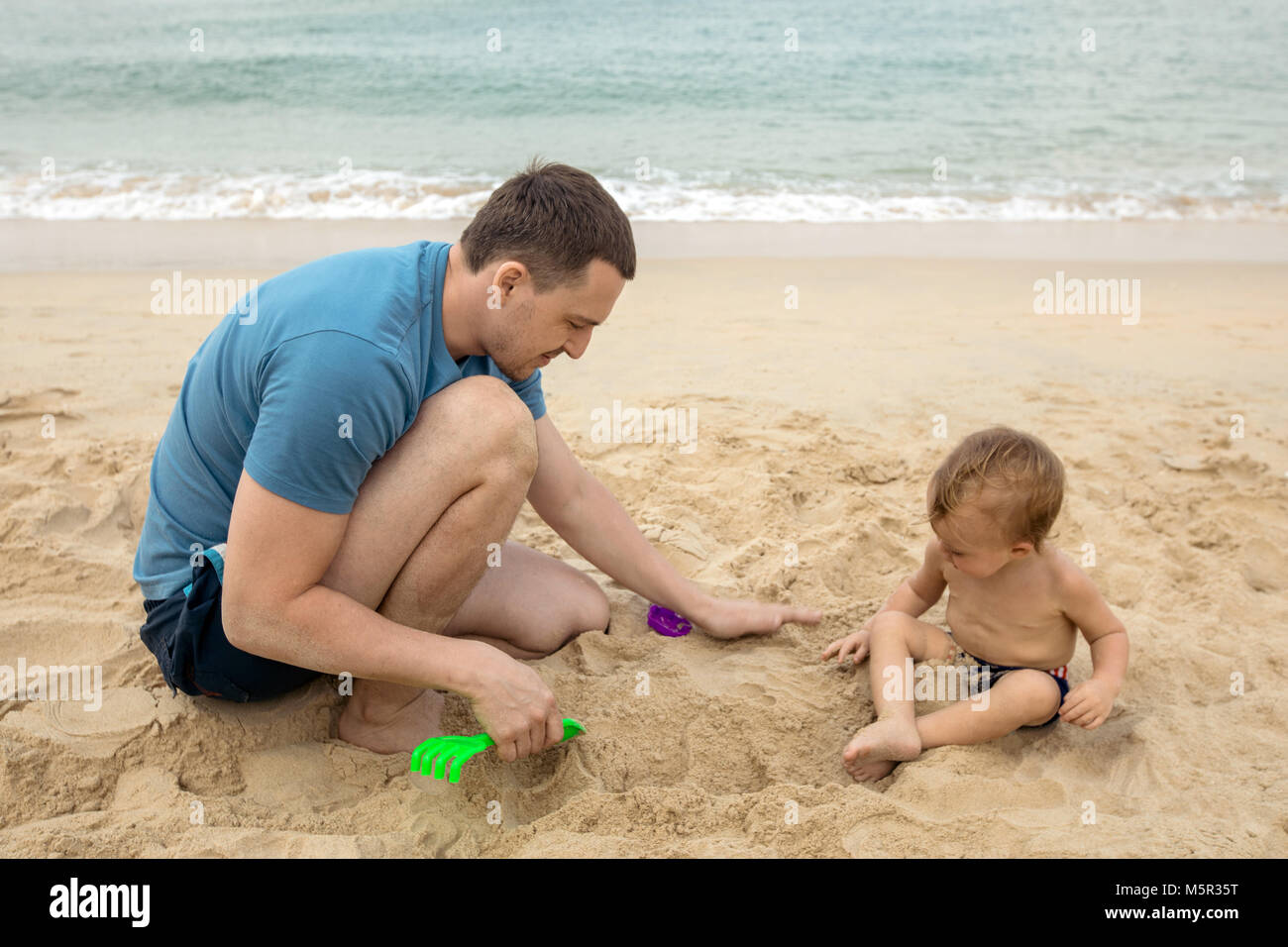 L'homme jouant avec bébé dans le sable Banque D'Images