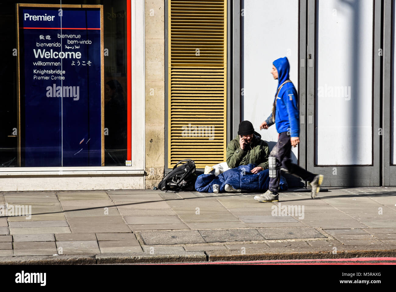 Homme sans abri au téléphone à Brompton Road, Knightsbridge, Londres dans la rue avec passer Banque D'Images